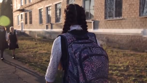Дівчата-підлітки в уніформі ходять до школи і зустрічаються з однокласницею. Вид ззаду. Задній — стокове відео