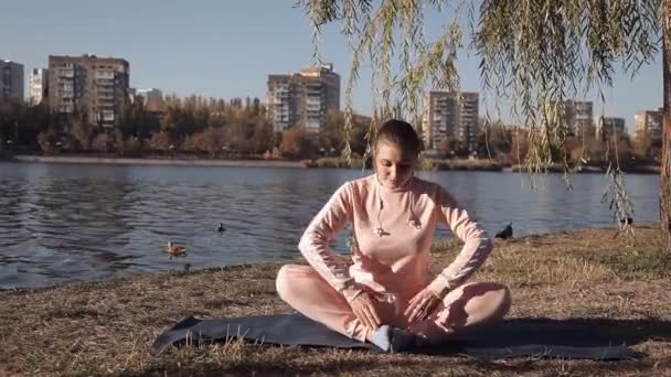 女の子が川の背景に公園でヨガ — ストック動画