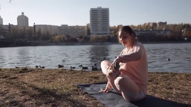 Holka dělá jógu v parku na pozadí řeky — Stock video