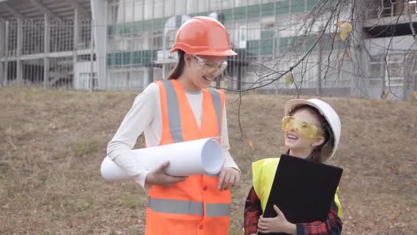 Δύο παιδιά κορίτσια σε Κράνη εργοταξίου βλέπουν λευκό φύλλο χαρτιού ή σχέδιο και χαμογελαστός — Αρχείο Βίντεο
