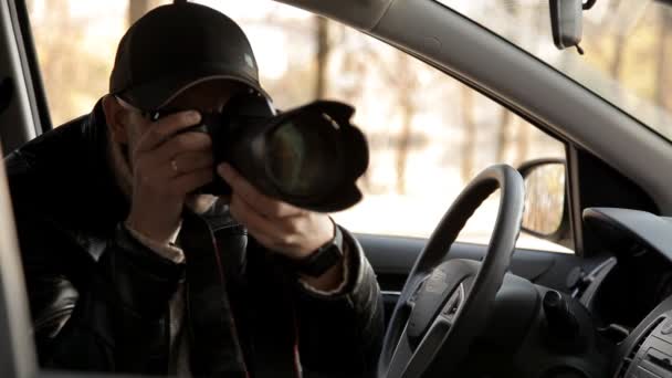 En privat detektiv eller en spion bedriver övervakning av föremålet för övervakning. En man i hemlighet tar bilder från bilfönstret — Stockvideo