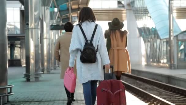 Achterzijde weergave passagiers met koffers wandelen op het perron van het station. Drie vrouwen met koffers wandelen op het perron van het station — Stockvideo