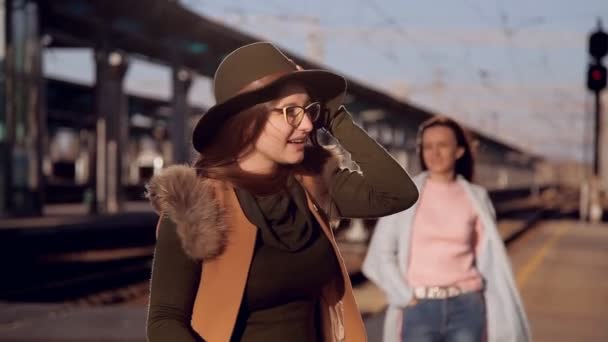 The wind blows off the girls hat. Girl in a hat and glasses at the railway station waiting for the train — Stock Video