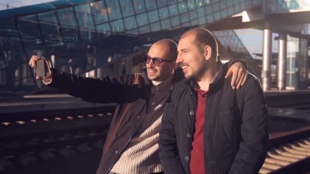 İki adam bir smartphone cep telefonu ile tren ve take resimleri selfie varış bekleyen tren istasyonu platformu — Stok video