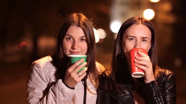 Dos chicas caminan por la noche en la ciudad charlando y tomando café — Vídeo de stock