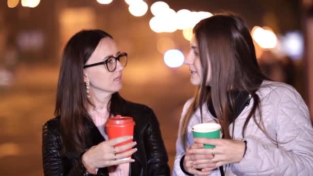 Две молодые девушки ходят по улицам незнакомого города осенним вечером и пьют кофе. — стоковое видео