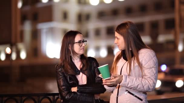 Twee jonge meisjes lopen door de oude stad bij nacht en chat, drinken warme koffie — Stockvideo