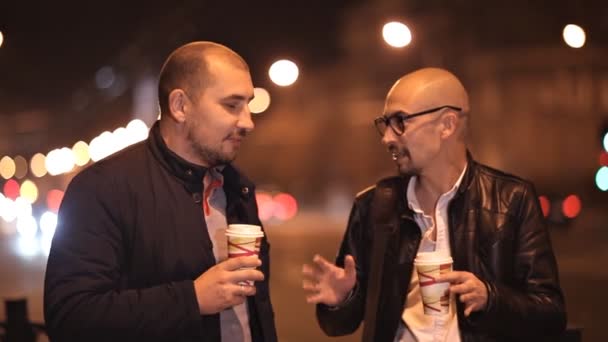 Två skalliga vänner vandrar på kvällen i staden chattar, dricka kaffe — Stockvideo