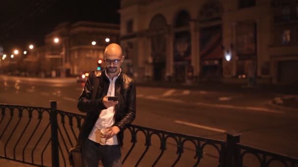 Aantrekkelijke jonge man wandelingen door de stad in de avond en drinkt koffie — Stockvideo