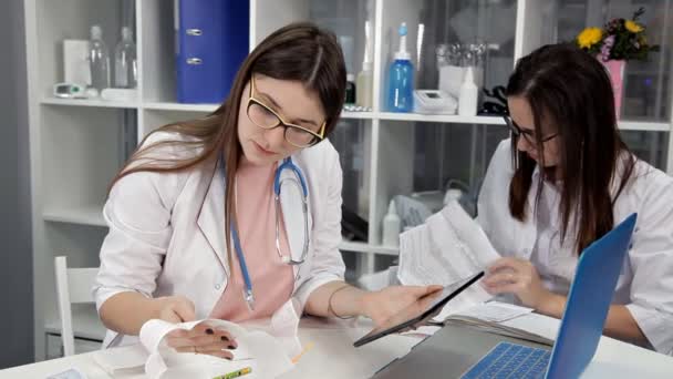 Las mujeres médicas trabajan en la mesa de la oficina con una computadora portátil y una tableta — Vídeo de stock