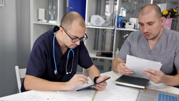 Junge Ärzte sitzen am Tisch im Büro und diskutieren die Behandlung und studieren die Notizen im Notizbuch — Stockvideo