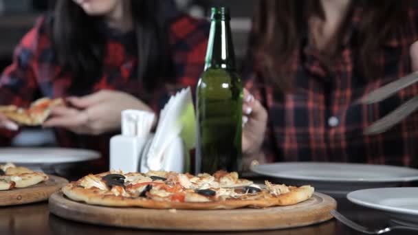 Несколько девушек едят пиццу и пьют пиво из бутылок в ресторане. Говорить смехом и праздновать — стоковое видео