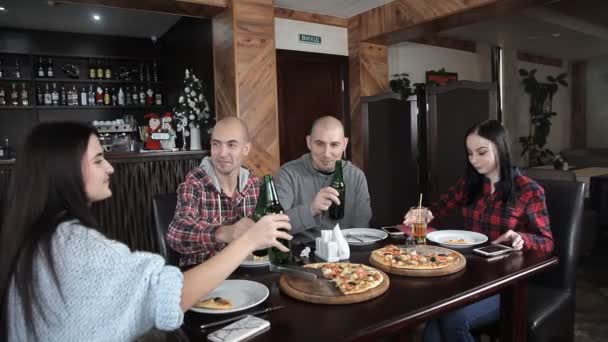 Un grupo de jóvenes bebe cerveza y come pizza en un restaurante — Vídeos de Stock