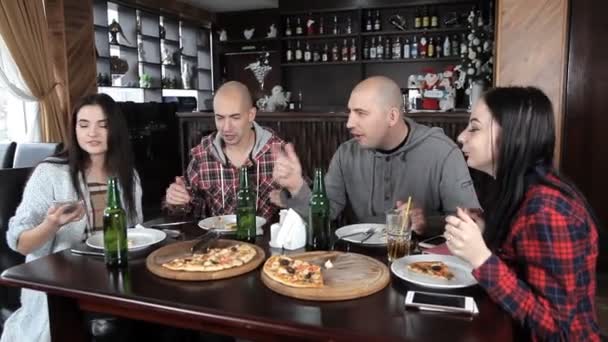 Un grupo de jóvenes bebe cerveza y come pizza en un restaurante — Vídeo de stock