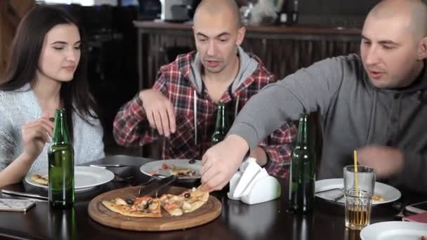 Група молодих людей п'ють пиво і їдять піцу в ресторані — стокове відео