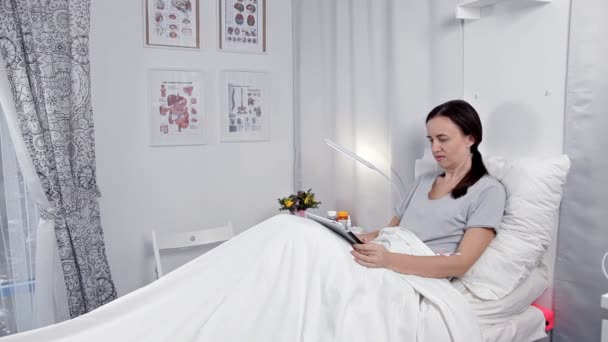 De patiënt ligt in de wijk, rust na de ingreep, maakt gebruik van de tablet — Stockvideo