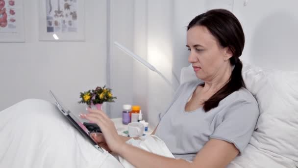 De patiënt ligt in de wijk, rust na de ingreep, maakt gebruik van de tablet — Stockvideo