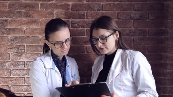 Dos doctoras revisan las notas médicas en un archivo y consultan sobre el diagnóstico. Trabajadores Sanitarios Profesionales Inteligentes. Adultos jóvenes blancos caucásicos — Vídeo de stock