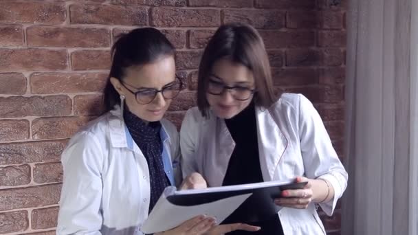 Duas médicas olham através das notas médicas em um arquivo e consultam no diagnóstico. Profissionais de Saúde Inteligentes. Branco Branco Branco Jovens Adultos — Vídeo de Stock