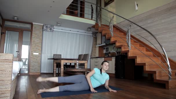 Joven mujer deportiva haciendo ejercicio en casa, haciendo ejercicios de fitness en el piso de la sala de estar utilizando el programa de entrenamiento personal en línea, haciendo pilates de yoga en el interior — Vídeos de Stock