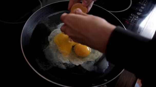 早上, 女孩在家里的厨房里准备早餐, 在煎锅里打破鸡蛋。特写。在家厨房煮鸡蛋 — 图库视频影像