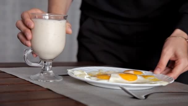 Молодая девушка приготовила яичницу на завтрак и положила ее на стол, и стакан молока — стоковое видео