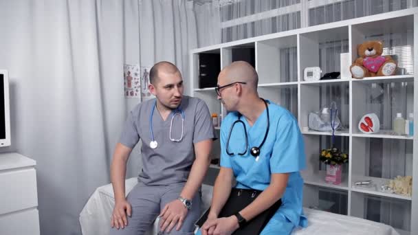 Мужчина-врач и молодой интерн в хорошем настроении говорят о новых медицинских исследованиях — стоковое видео