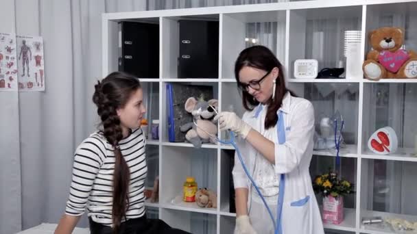 Молодой врач осматривает пациента, ребенка, в своем кабинете — стоковое видео