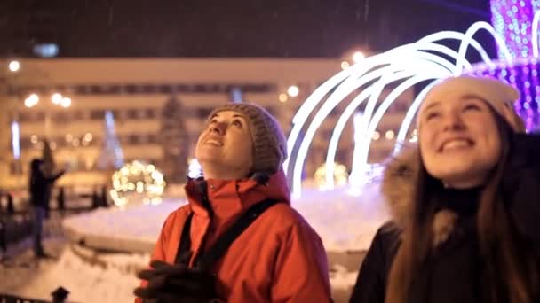 Jóvenes niñas felices cerca de las luces de colores y guirnaldas en la ciudad de la noche — Vídeo de stock