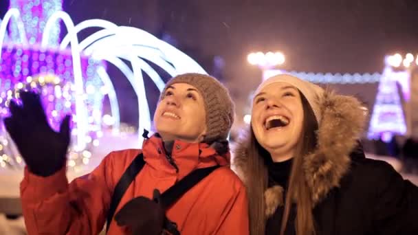 Jóvenes niñas felices cerca de las luces de colores y guirnaldas en la ciudad de la noche — Vídeo de stock