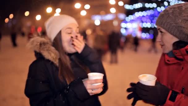 Молодые девушки пьют кофе в парке, смеются. Зимняя погода снаружи. Перерыв на кофе. Рождество — стоковое видео