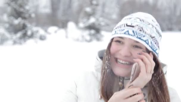 一个年轻女孩在冬天的雪中散步, 在电话里说话 — 图库视频影像