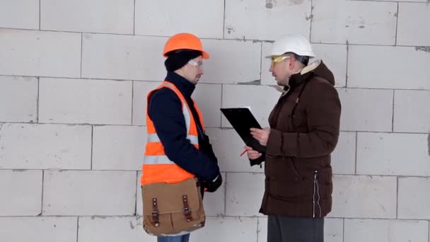 Un ingénieur et un architecte discutent d'un plan de projet. Ils ont un casque de protection sur la tête. Travail, projet — Video