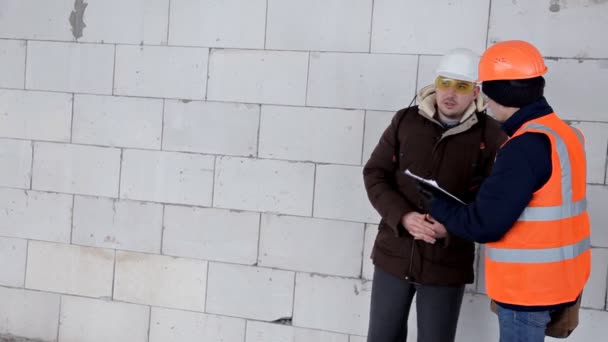 El cliente en un casco de protección verifica el trabajo de los constructores en el objeto en construcción, la gente camina a través del edificio de la antigua fábrica — Vídeo de stock