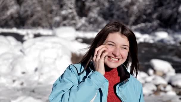 Das Mädchen in der blauen Jacke geht an einem sonnigen Wintertag am See im Wald spazieren und telefoniert — Stockvideo