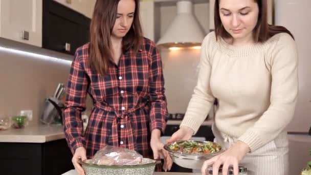 Twee jonge meisjes zet kip in bakken en cadeauzakje. Heerlijke kip diner — Stockvideo