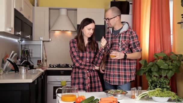 O cara e a menina conversam na cozinha e riem enquanto a comida está preparada — Vídeo de Stock