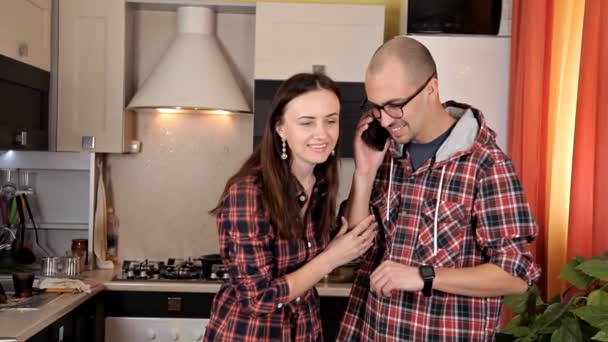 A young couple sets the table, preparing for dinner. Plates, juice, food. Talking on the phone in the kitchen — Stock Video