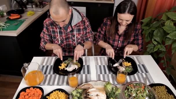 Marito e moglie si siedono in cucina a tavola e cenano. Sul tavolo, insalata, verdure, verdure, pollo, mais. Cibo fatto in casa — Video Stock