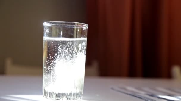 Ο άνθρωπος ρίχνει αναβράζον δισκίο σε ένα ποτήρι νερό στο τραπέζι — Αρχείο Βίντεο