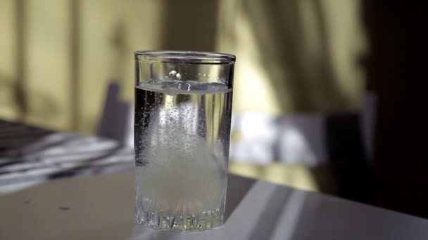 Чоловік кидає випромінювальну таблетку в склянку води за столом — стокове відео