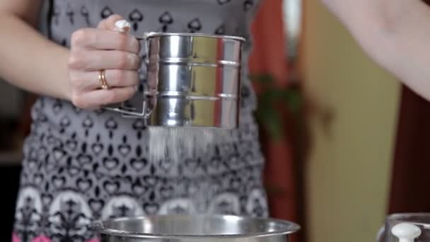 En kvinna sållar mjölet genom en metall sieve kopp i köket. Begreppet av matlagning och bakning — Stockvideo