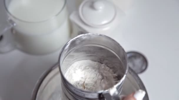Una mujer tamiza la harina a través de una taza de tamiz de metal en la cocina. El concepto de cocinar y hornear — Vídeo de stock