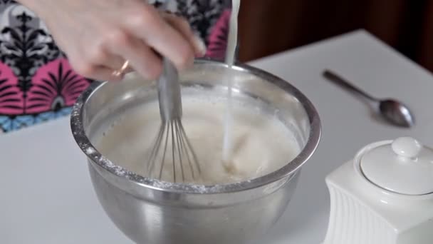 En kvinna häller mjölk från en kopp i en skål med degen. Flickan förbereder pannkakor, cookies, degen — Stockvideo
