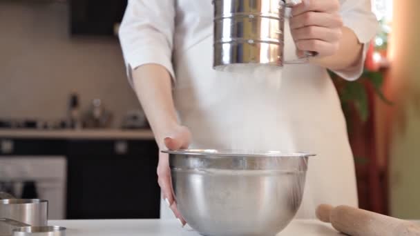 A young woman in a white apron sifts the flour through a sieve to make pizza dough — Stock Video