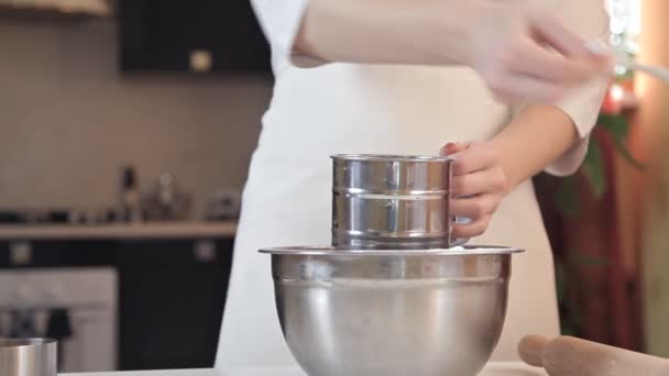 A young woman in a white apron sifts the flour through a sieve to make pizza dough — Stock Video