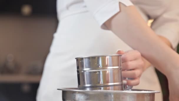 Una mujer joven en un delantal blanco tamiza la harina a través de un tamiz para hacer masa de pizza — Vídeos de Stock