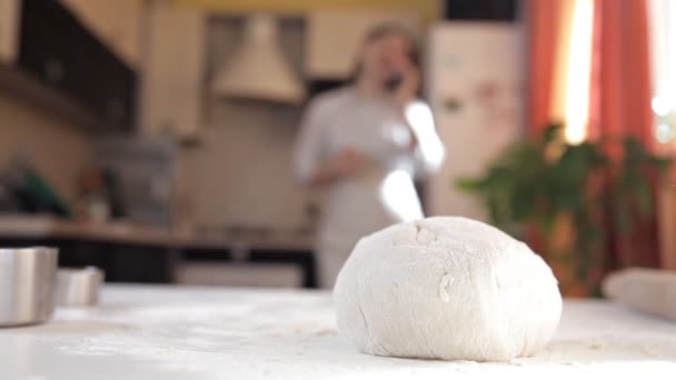 Ein junges Mädchen in der Küche bereitete den Teig zum Backen zu. der Teig auf dem Tisch, das Mädchen telefoniert — Stockvideo