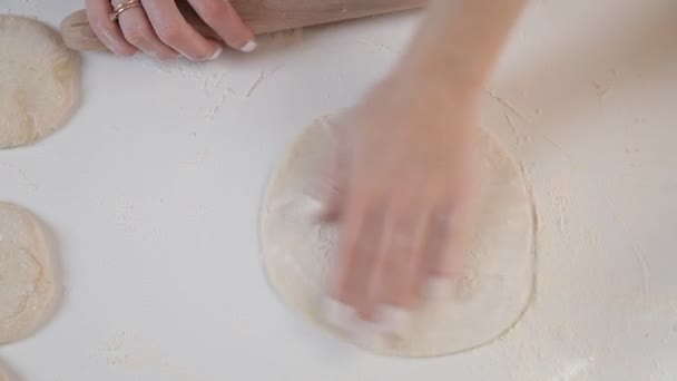 Mujer panadero rueda la masa con un rodillo sobre un fondo de ingredientes en una mesa de madera y harina — Vídeos de Stock
