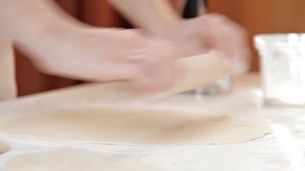 Mujer panadero rueda la masa con un rodillo sobre un fondo de ingredientes en una mesa de madera y harina — Vídeos de Stock